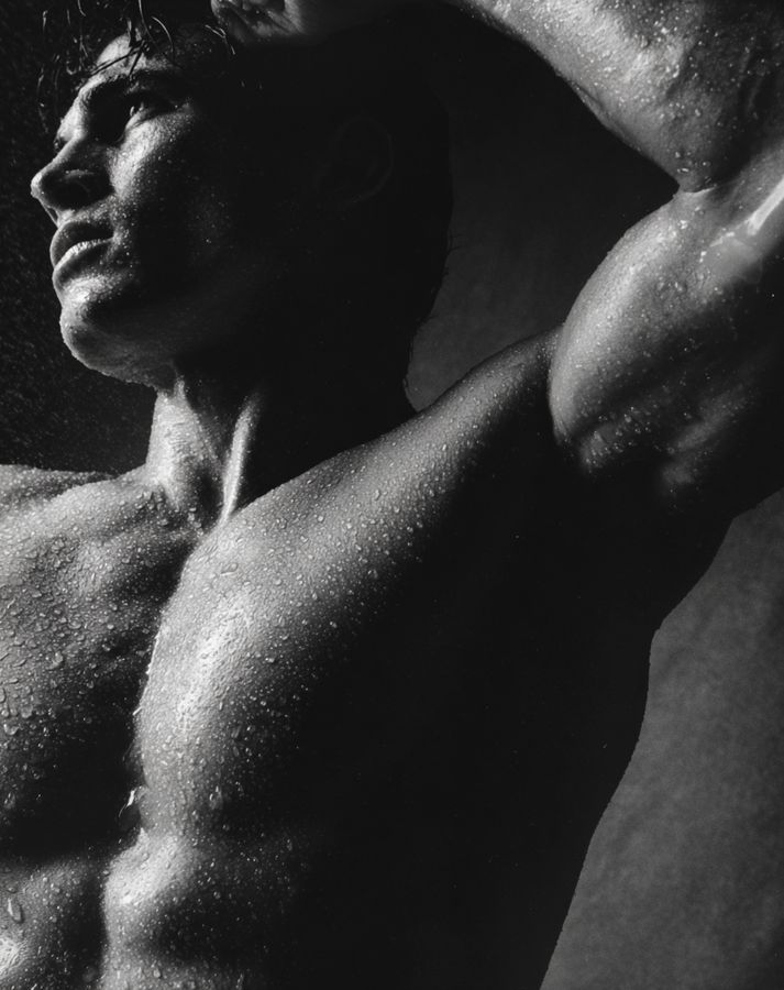 A man stretching with one arm raised, in black and white