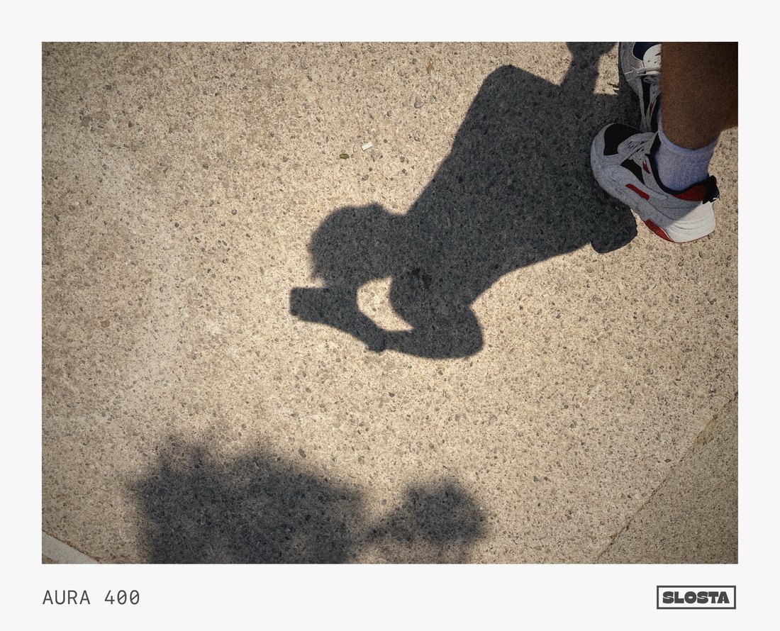 An overhead shadow cast on sunlit pavement, framed with SloSta's AURA 400 film stock