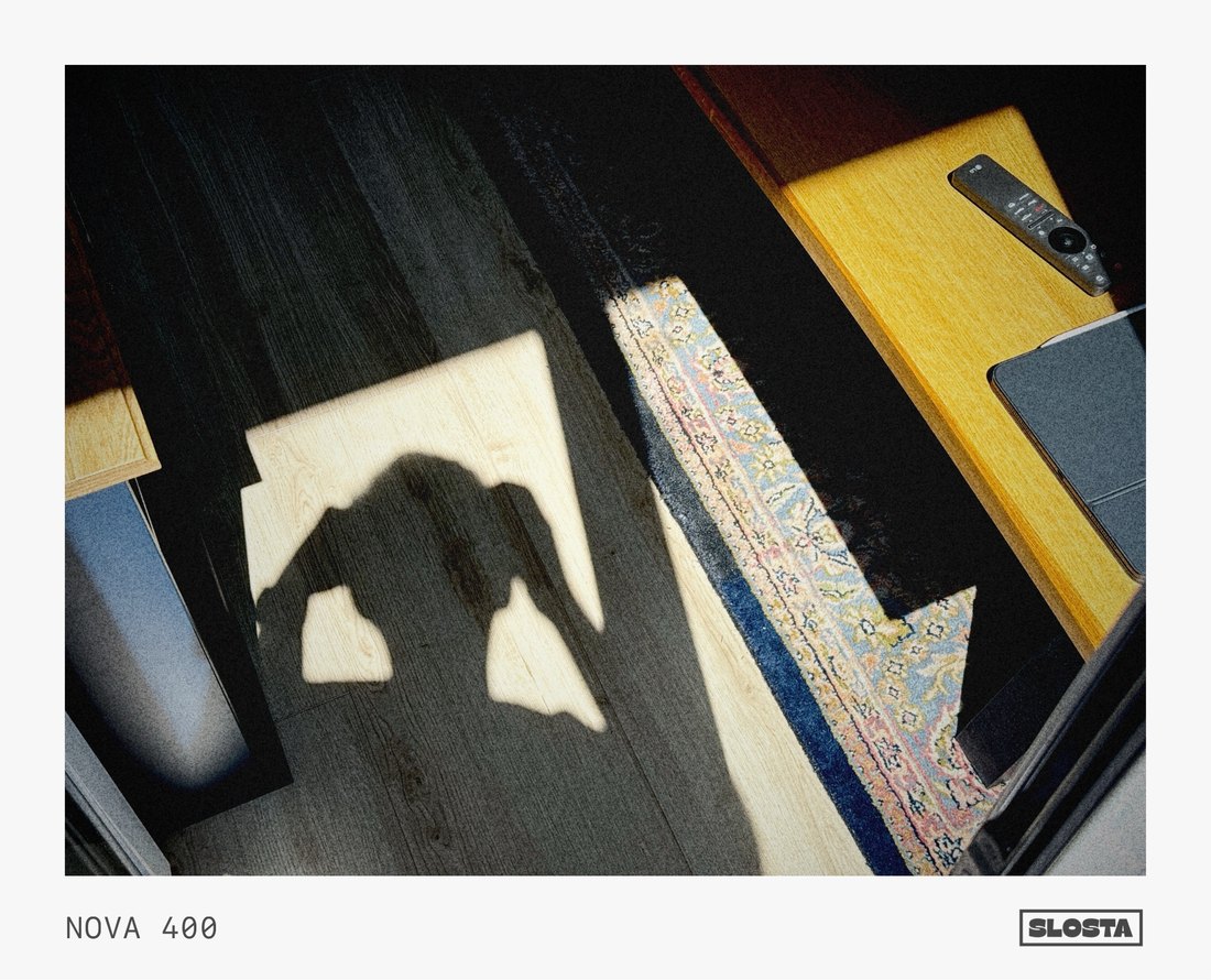 An overhead shot of a sunlit wooden floor and Persian rug, with a person's shadow cast across it, framed with SloSta's NOVA 400 film stock