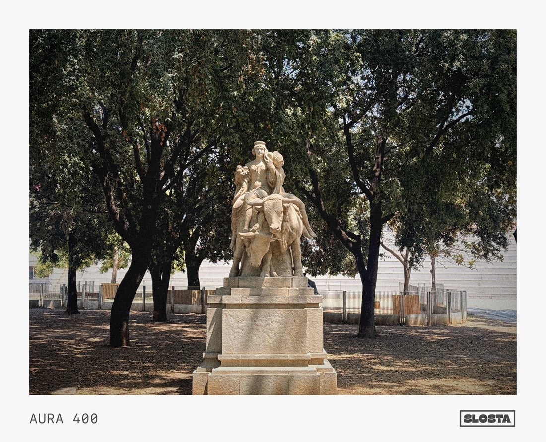 A stone statue in a tree-lined park, framed with SloSta's AURA 400 film stock